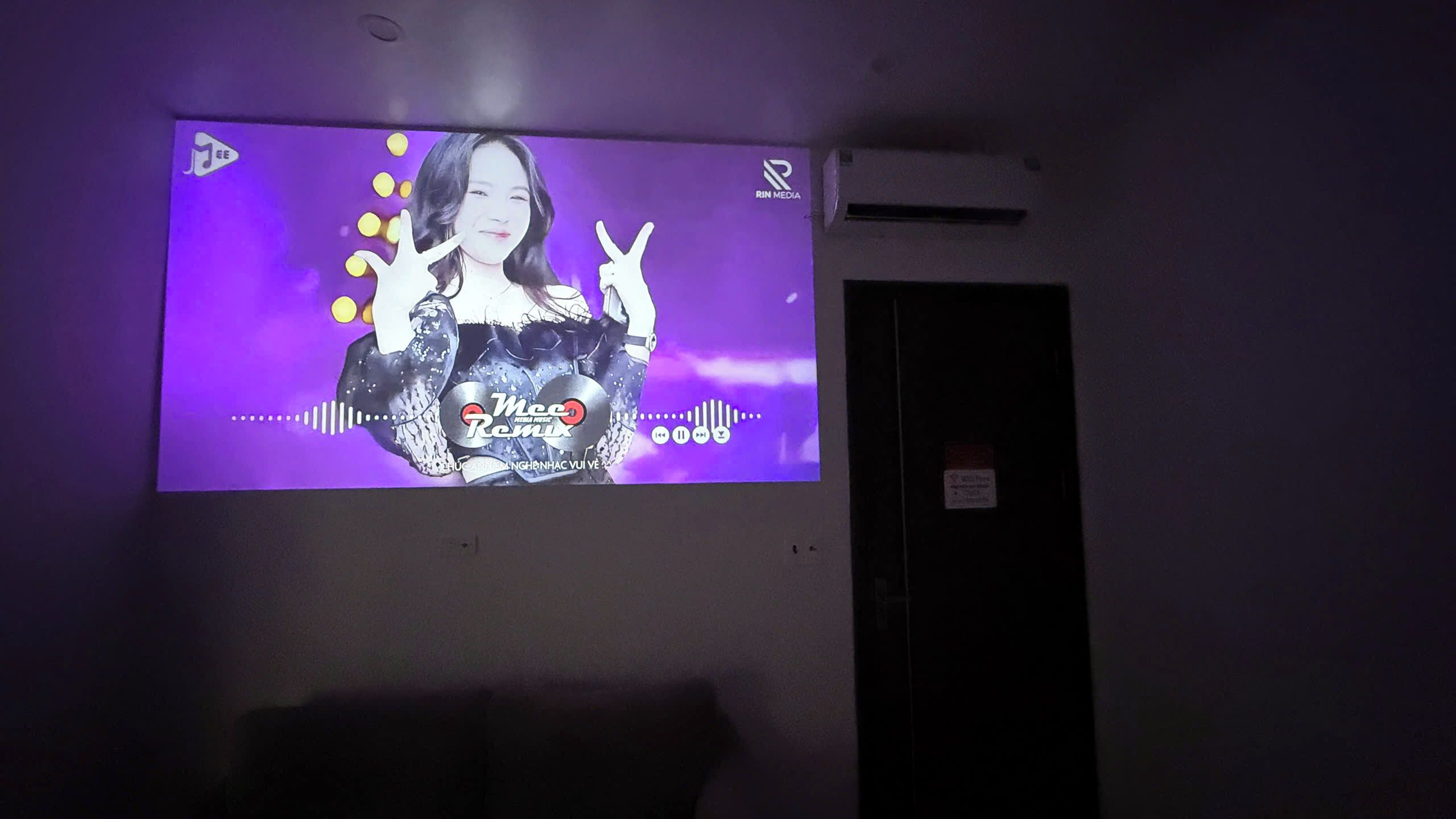 A projection screen displaying a music video with a person making a peace sign.
