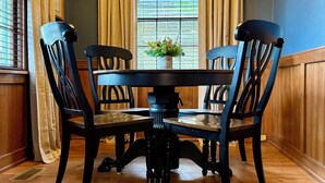 Un comedor con una mesa redonda y cuatro sillas, una planta en maceta sobre la mesa, y una ventana con persianas.