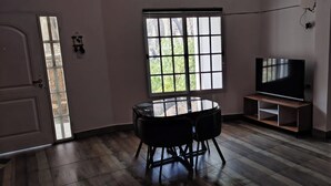 Un salon avec une table ronde, un canapé, un téléviseur posé sur un meuble et une fenêtre donnant sur un paysage verdoyant.