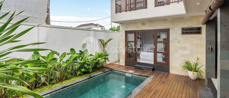 Una casa moderna de dos pisos con piscina, terraza de madera y plantas en macetas.