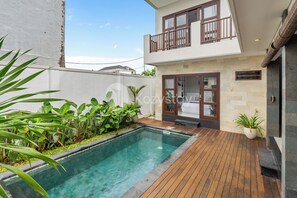 Una casa moderna de dos pisos con piscina, terraza de madera y plantas en macetas.