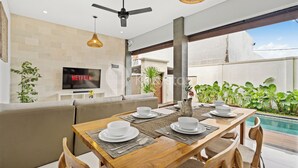 A modern dining area with a wooden table set for four, a sofa, and a TV displaying 'NETFLIX'. - Cavara Villa by Kozystay - Ungasan (Ungasan)
