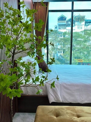 A hotel room with a bed, a window with a view of buildings, and a plant.