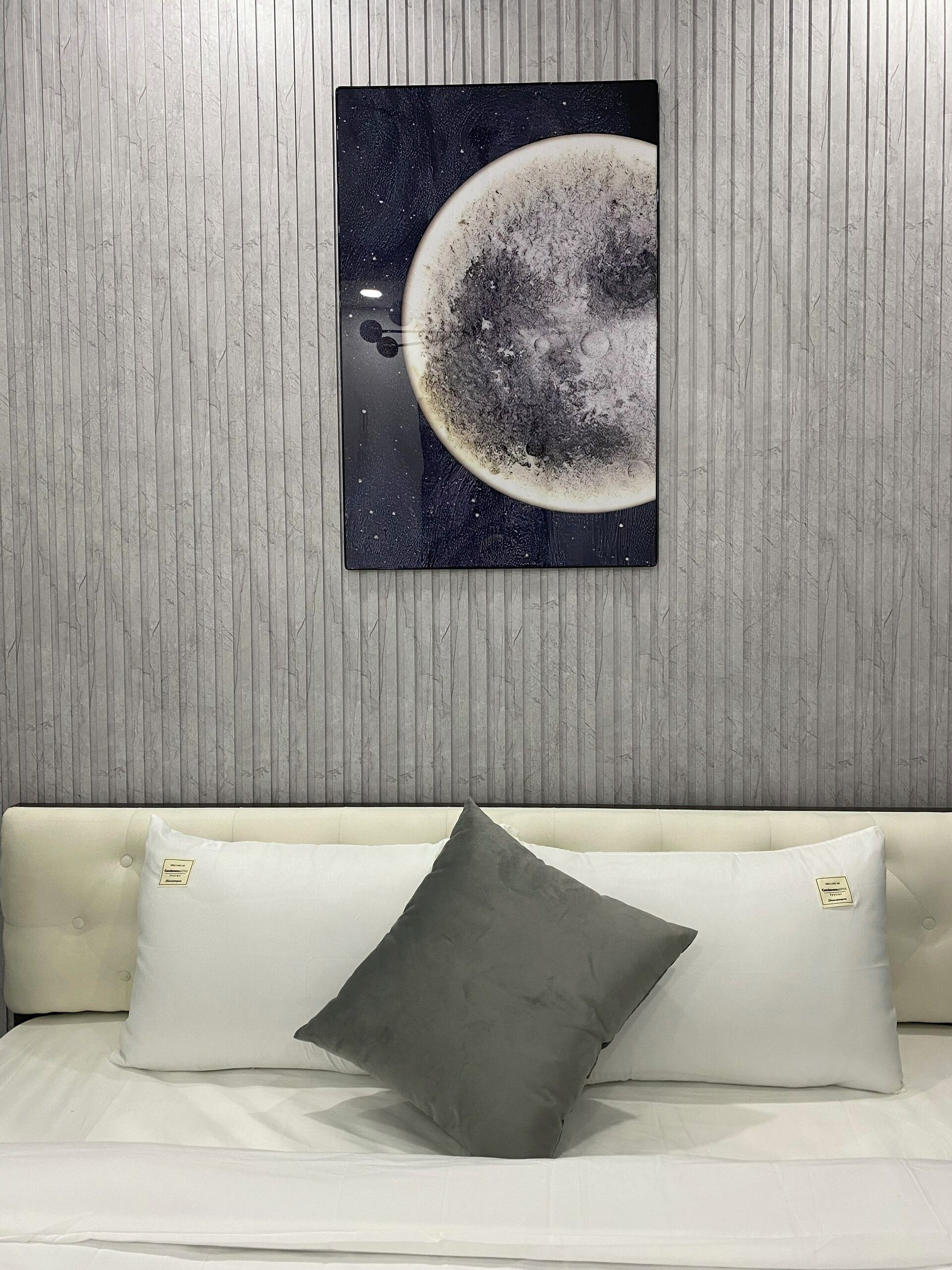 Una habitación con una obra de arte colgada en la pared que representa la luna, un sofá blanco con dos cojines y una pared con textura.