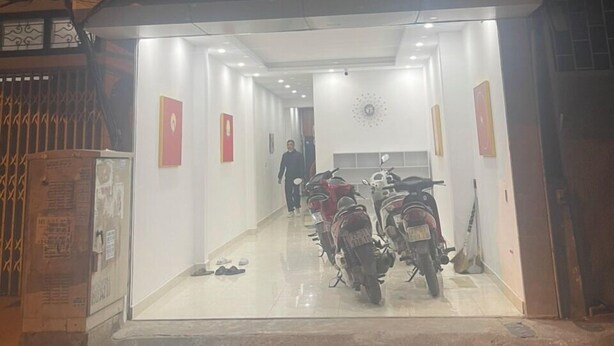 A building entrance with a glass door, a person walking inside, and several parked scooters. - Grand C Homestay (Hanoi)
