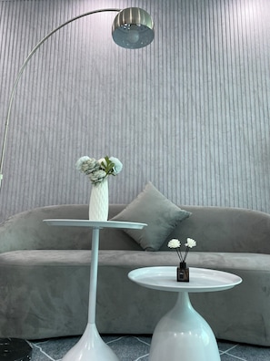 Een moderne woonkamer met een grijze bank, een witte vaas met bloemen, een witte tafel en een vloerlamp.