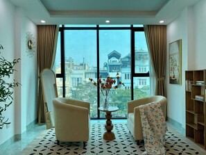 Una habitación con dos sillones, una mesa redonda y vistas a edificios a través de amplios ventanales.