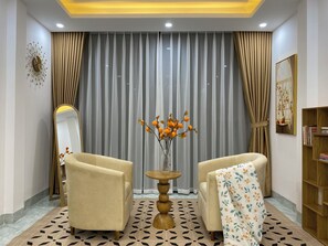 Una habitación con dos sillones, una mesa redonda de madera con un jarrón de flores naranjas, un espejo y una estantería.
