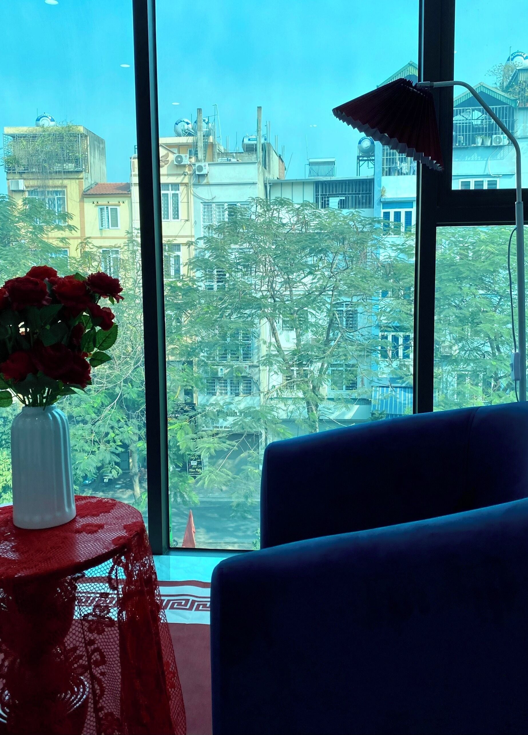 Una habitación con un ventanal grande, una mesa roja con un florero y una silla azul.