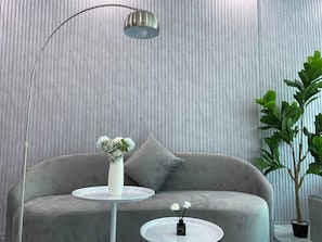 A modern living room with a grey sofa, a white vase with flowers, a small table, and a tall plant. - Grand C Homestay (Hanoi)