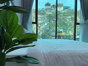 A hotel room with a large bed, curtains, and a view of buildings and trees outside the window.