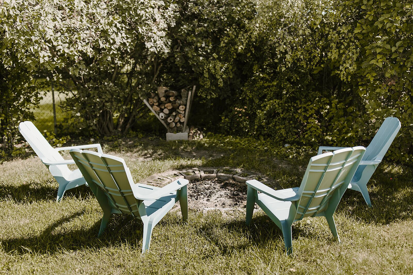 Un foyer extérieur entouré de quatre chaises Adirondack, le tout installé dans un espace extérieur verdoyant.
