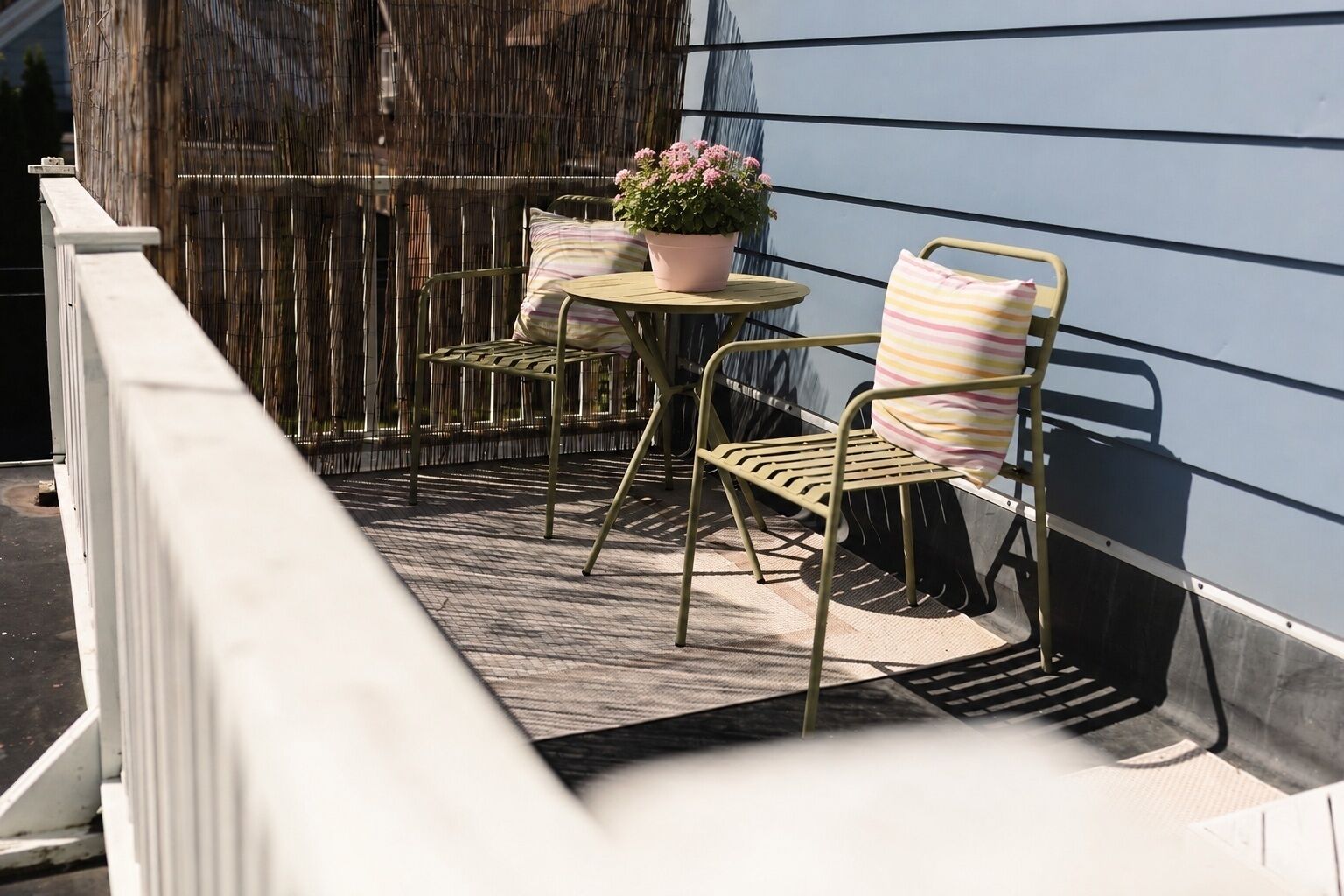 Un balcon avec une chaise en métal, une petite table ronde et un pot de fleurs.
