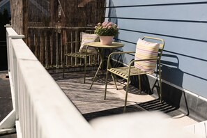 Ein Balkon mit einem Metallstuhl, einem kleinen runden Tisch und einem Blumentopf.