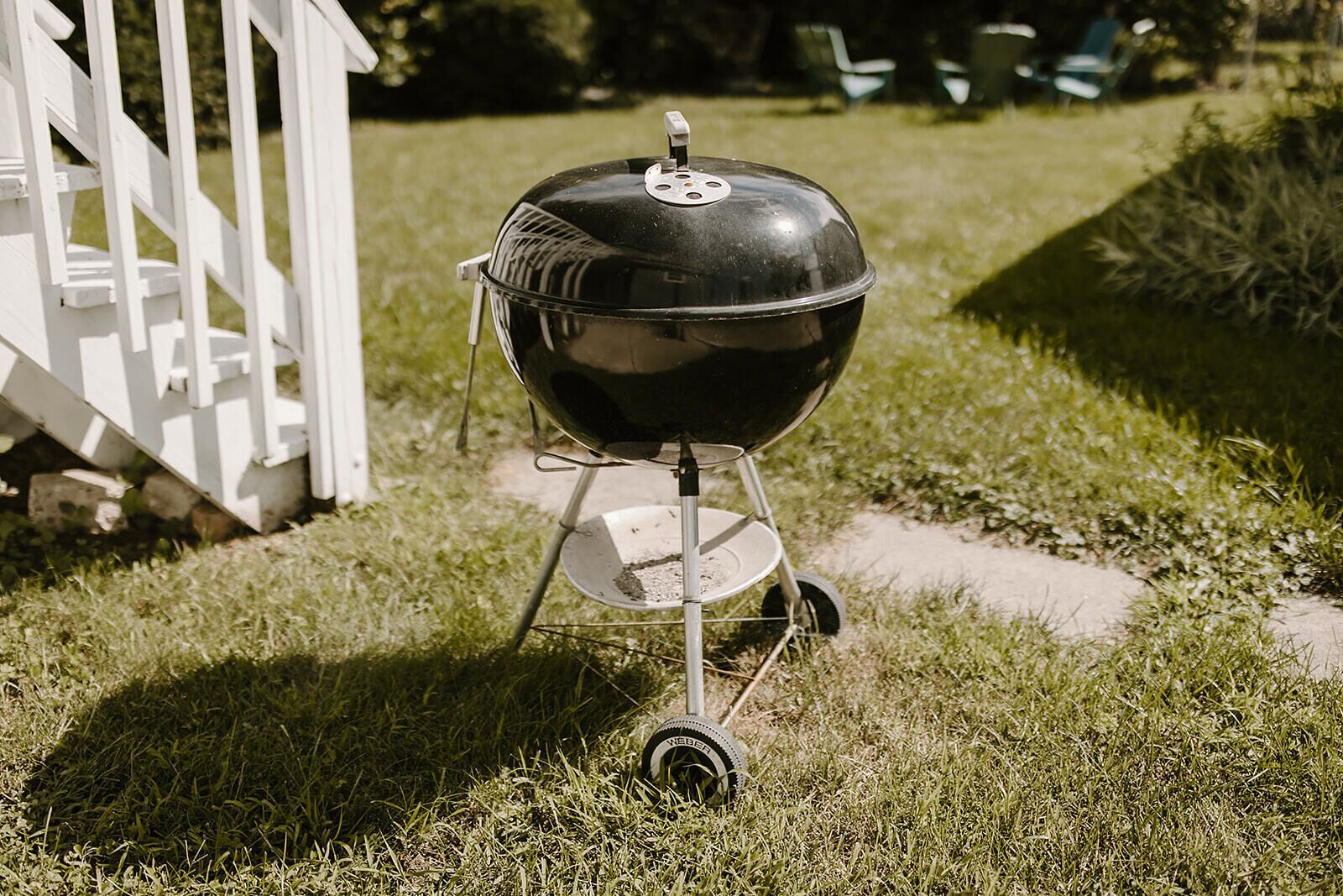 Un barbecue portable sur une pelouse verdoyante, avec une clôture blanche en arrière-plan.