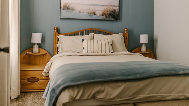 Un dormitorio con cama de madera, dos mesitas de noche con lámparas, un cuadro en la pared y suelo alfombrado.