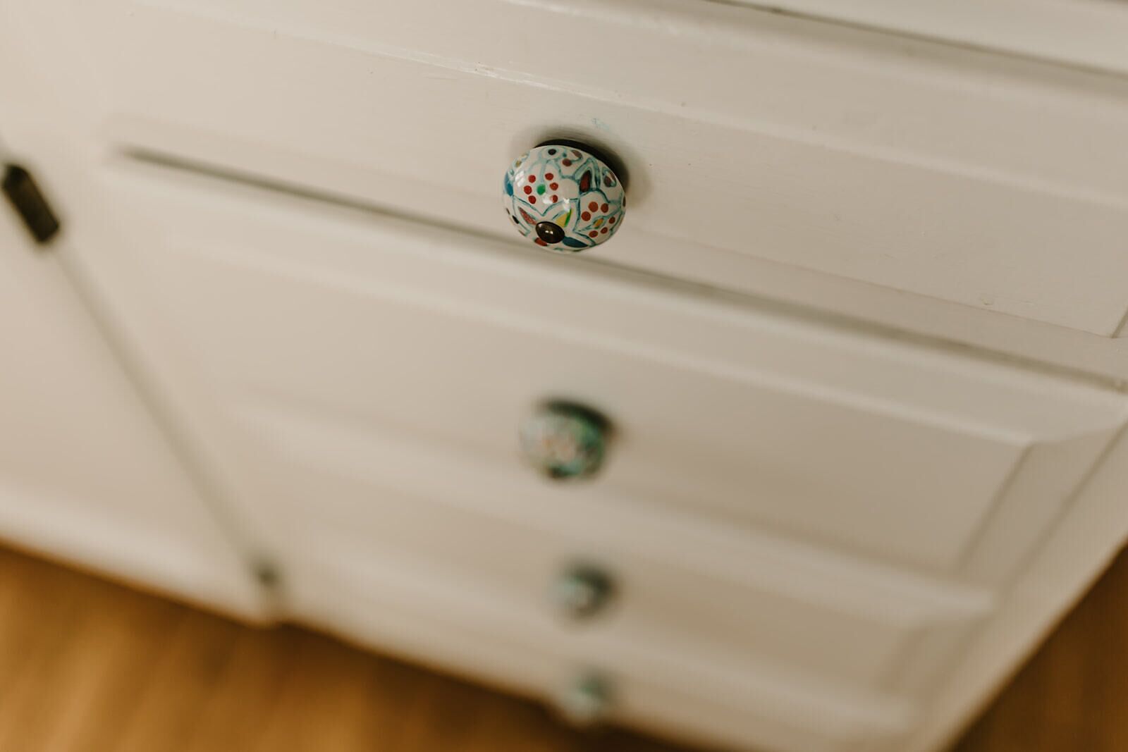 Uma cómoda branca com uma puxaça decorativa e três gavetas.