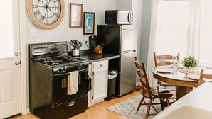 Cocina compacta con estufa, horno, microondas y refrigerador. Hay una mesa de comedor con sillas y un reloj en la pared.