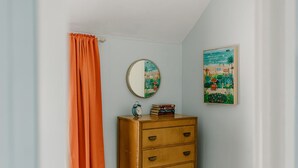 Una habitación con un aparador de madera, un espejo, un reloj y un cuadro en la pared.