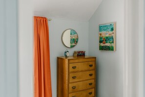 A room with a wooden dresser, a mirror, a clock, and a framed painting on the wall.