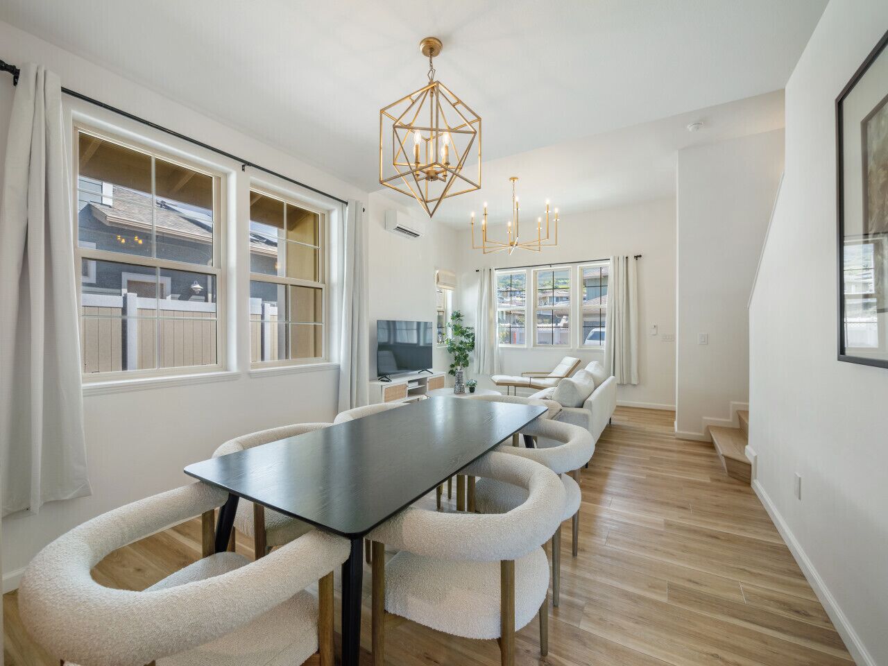 A modern dining area with a long table, cushioned chairs, and a geometric chandelier.