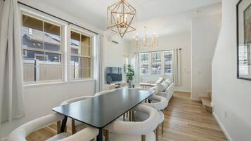 A modern dining area with a long table, cushioned chairs, and a geometric chandelier.