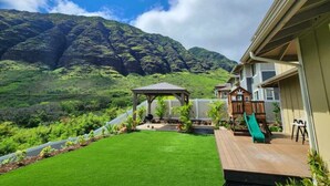 A backyard with a wooden deck, a gazebo, a playhouse, and a green lawn. - Ocean Views|Outdoor Kids Play Set|BBQ|Beach 6 Min (Waianae)