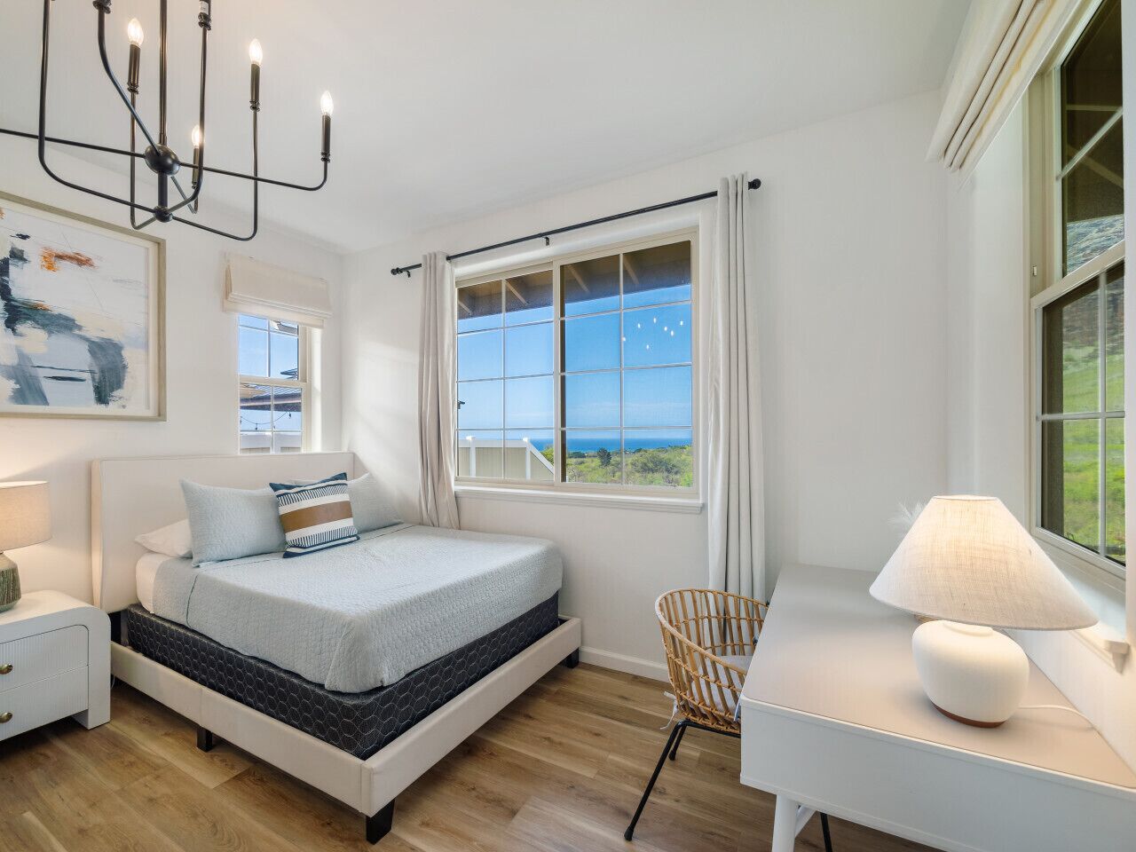 A bedroom with a bed, bedside table, lamp, chair, and a window with a view.