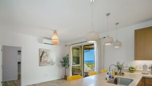 A modern kitchen with a large island, pendant lights, and a view of the ocean.