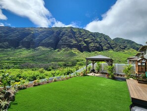A well-maintained lawn with a gazebo, a wooden deck, and a view of lush green hills and mountains.