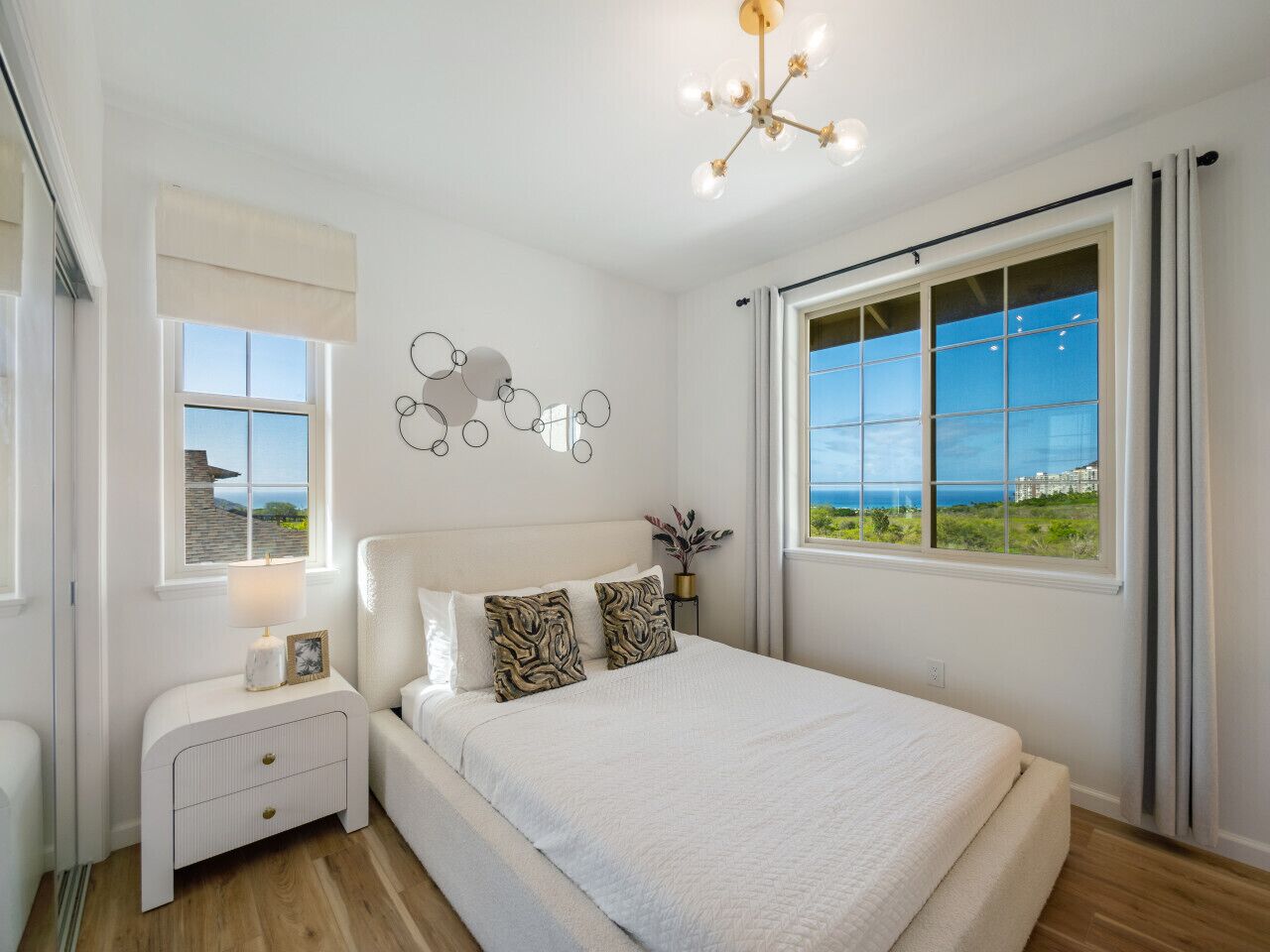 Ein Schlafzimmer mit einem großen Bett, einem Nachttisch, einer Wandleuchte und einem Fenster mit Blick aufs Meer.