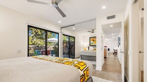 Un dormitorio moderno con una cama grande, un ventilador de techo y vistas al exterior a través de puertas de vidrio.
