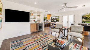 Una sala de estar moderna con un televisor de pantalla plana, un comedor con mesa y sillas, y una cocina con armarios y encimera.