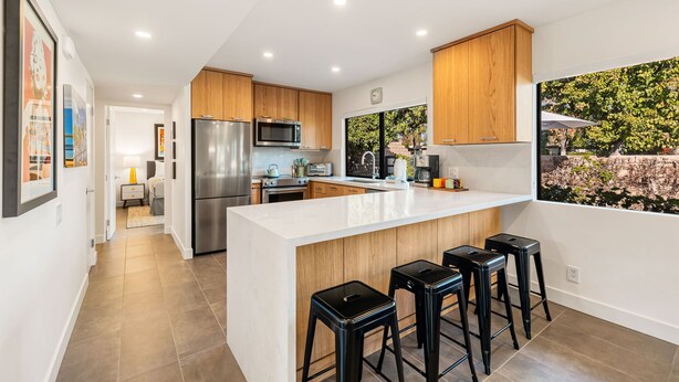 Una cocina moderna con una isla grande, armarios de madera, electrodomésticos de acero inoxidable y vistas a un jardín.
