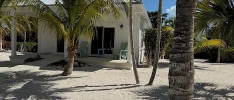 A beach house with a covered patio, palm trees, and a sandy beach.