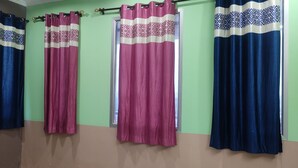 A room with four curtains, two blue and two pink, hanging on a wall with a window. - Shree Vishvakarma Resorts (Taranagar)