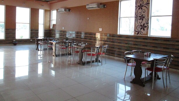 A spacious dining area with multiple tables and chairs, large windows, and a decorative ceiling design. - Shree Vishvakarma Resorts (Taranagar)