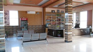 A lobby with a seating area, a Coca-Cola refrigerator, a counter with various items, and a tiled floor. - Shree Vishvakarma Resorts (Taranagar)