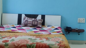 A bedroom with a bed, air conditioning unit, and a small shelf with a phone and charger. - Shree Vishvakarma Resorts (Taranagar)