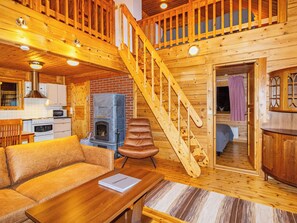 A cozy cabin interior with a wooden staircase, a fireplace, a sofa, and a dining area.