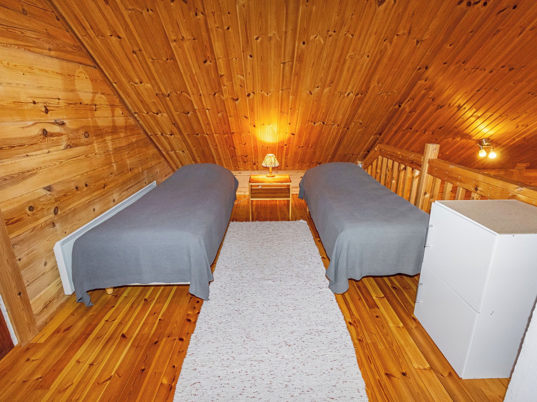 Une chambre confortable située dans les combles, avec des murs en bois, deux lits simples, une table de chevet et une lampe.