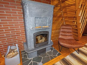 Una chimenea de piedra con un banco de madera y una silla en una habitación con paredes de madera y un tapete estampado.