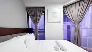 A hotel room with a large bed, two windows with curtains, a headboard, and a wall-mounted light fixture.