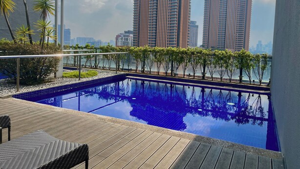 A rooftop pool with a view of high-rise buildings, surrounded by trees and a wooden deck.