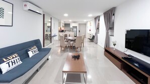 A modern living room with a sofa, coffee table, TV, and a dining area in the background.