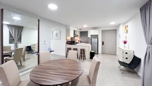 A modern hotel room with a dining area, kitchenette, and a separate living space.