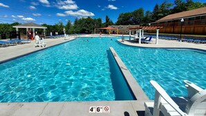 En swimmingpool med klart, blåt vand, omgivet af liggestole og parasoller, og et livredder-tårn i baggrunden.