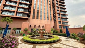 Een modern gebouw met een centrale fontein, omringd door groen en een vloer van decoratieve tegels.