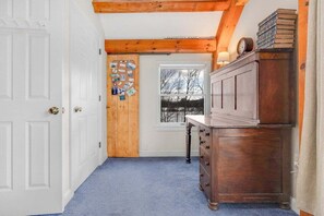 Een hal met een houten plafond, een witte deur, een blauw tapijt en een houten dressoir met boeken.