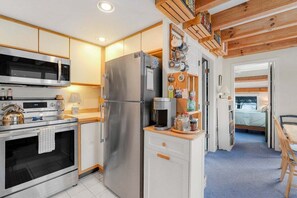 Een kleine keuken met moderne apparatuur, een eethoek met een houten tafel, en een zichtbare slaapkamer met een bed.